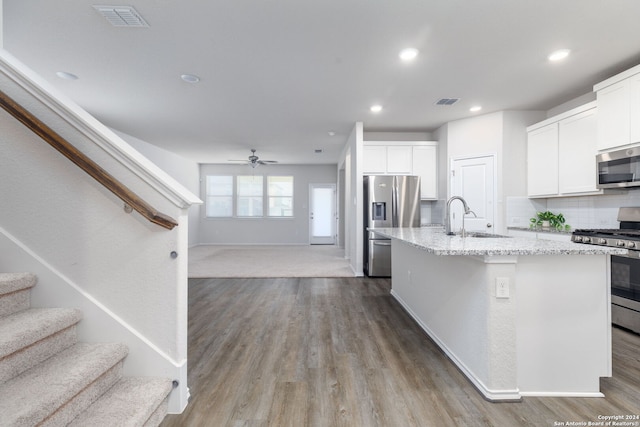 kitchen featuring light stone countertops, appliances with stainless steel finishes, tasteful backsplash, white cabinets, and an island with sink