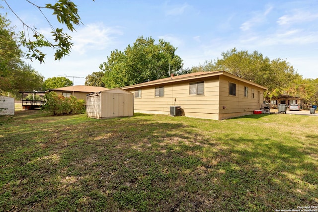 rear view of house with central AC unit, a storage shed, and a yard