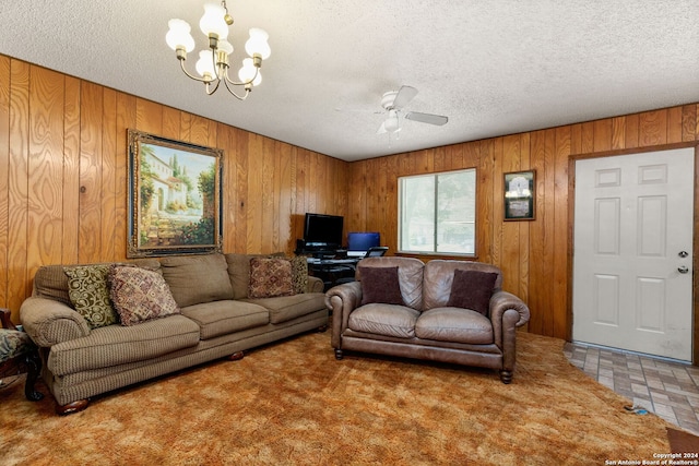 carpeted living room featuring ceiling fan with notable chandelier, wood walls, and a textured ceiling