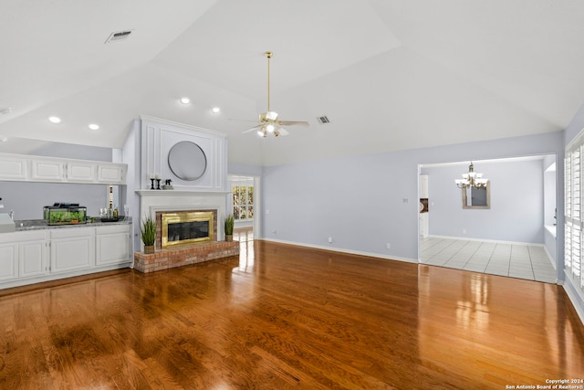 unfurnished living room featuring vaulted ceiling, a fireplace, hardwood / wood-style floors, and ceiling fan with notable chandelier