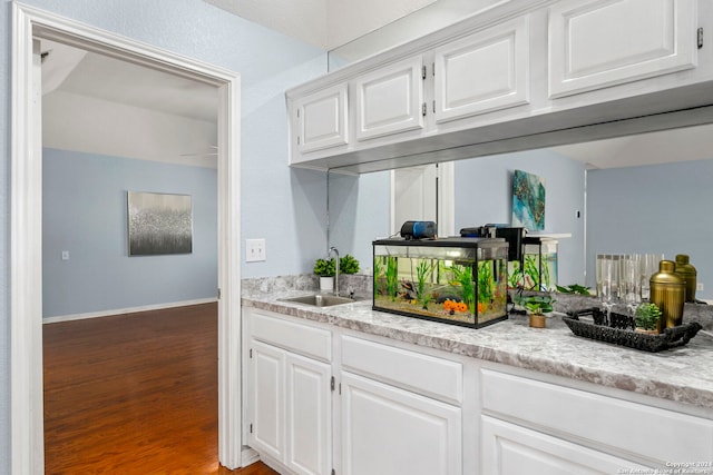 kitchen with light stone countertops, white cabinetry, sink, and hardwood / wood-style floors