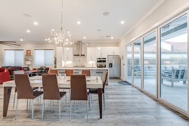 dining space featuring sink, ornamental molding, ceiling fan with notable chandelier, and light wood-type flooring