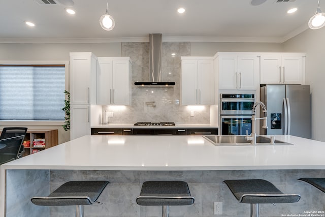 kitchen featuring white cabinets, stainless steel appliances, a center island with sink, and wall chimney range hood