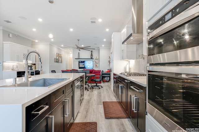 kitchen featuring pendant lighting, wall chimney exhaust hood, light wood-type flooring, appliances with stainless steel finishes, and white cabinetry