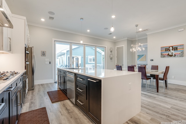 kitchen with appliances with stainless steel finishes, a kitchen island with sink, sink, pendant lighting, and light hardwood / wood-style flooring