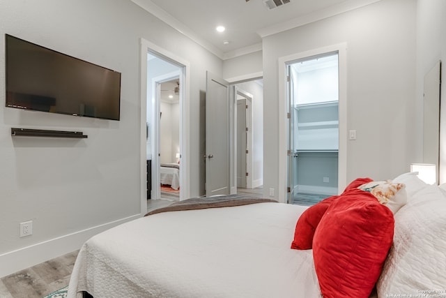 bedroom with crown molding, hardwood / wood-style floors, ensuite bathroom, and a spacious closet