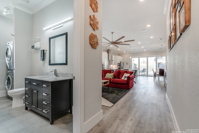 interior space with vanity, crown molding, toilet, stacked washing maching and dryer, and wood-type flooring