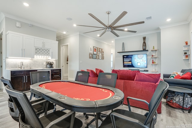 dining room featuring indoor wet bar, light hardwood / wood-style flooring, ceiling fan, and crown molding