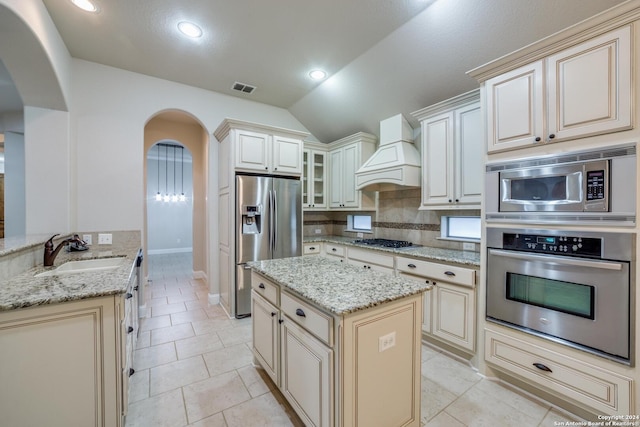 kitchen with light stone countertops, appliances with stainless steel finishes, premium range hood, vaulted ceiling, and sink