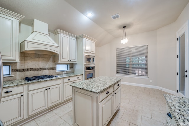 kitchen with light stone counters, pendant lighting, lofted ceiling, a kitchen island, and appliances with stainless steel finishes