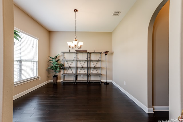 unfurnished dining area featuring dark wood-type flooring and an inviting chandelier