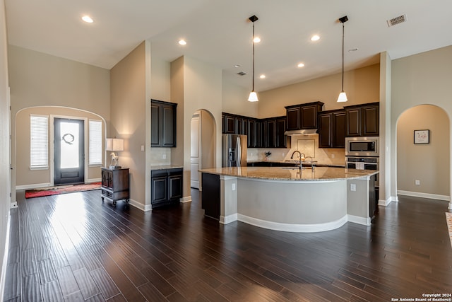 kitchen with a spacious island, hanging light fixtures, a towering ceiling, and stainless steel appliances