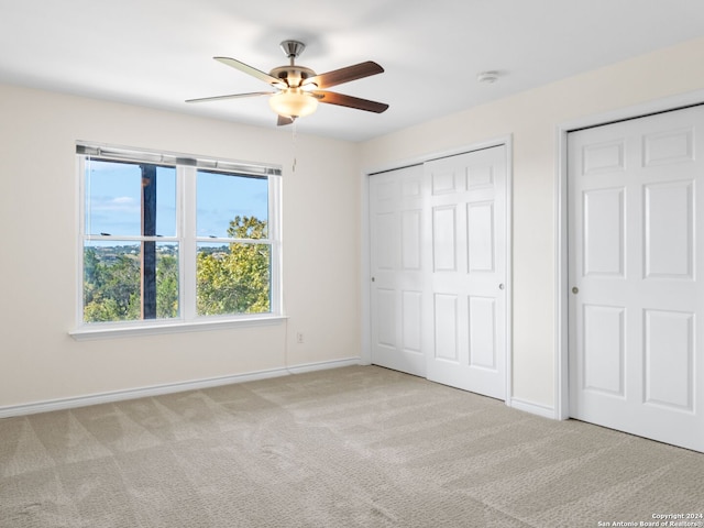 unfurnished bedroom featuring ceiling fan, light carpet, and two closets