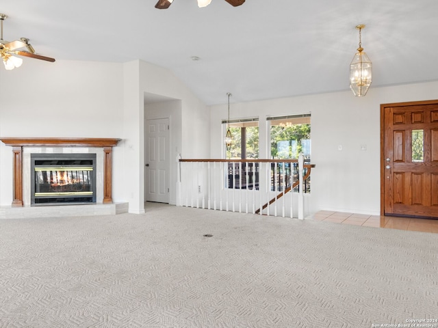 unfurnished living room featuring ceiling fan with notable chandelier, light colored carpet, and vaulted ceiling