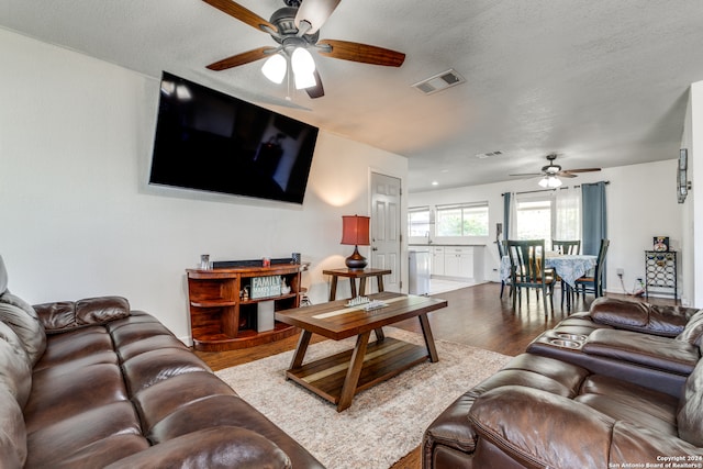 living room featuring hardwood / wood-style flooring, ceiling fan, and a textured ceiling