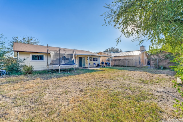 rear view of house featuring a lawn, a trampoline, and a patio