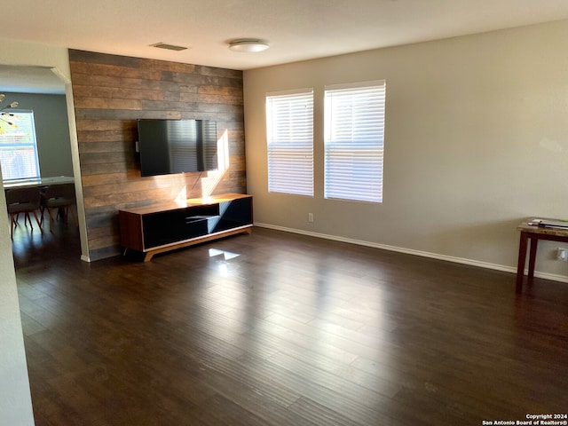 unfurnished living room featuring wooden walls, dark wood-type flooring, and an inviting chandelier