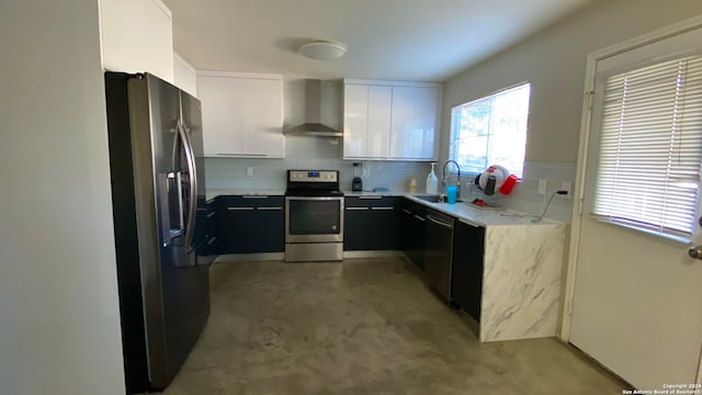 kitchen with appliances with stainless steel finishes, tasteful backsplash, wall chimney exhaust hood, sink, and white cabinets