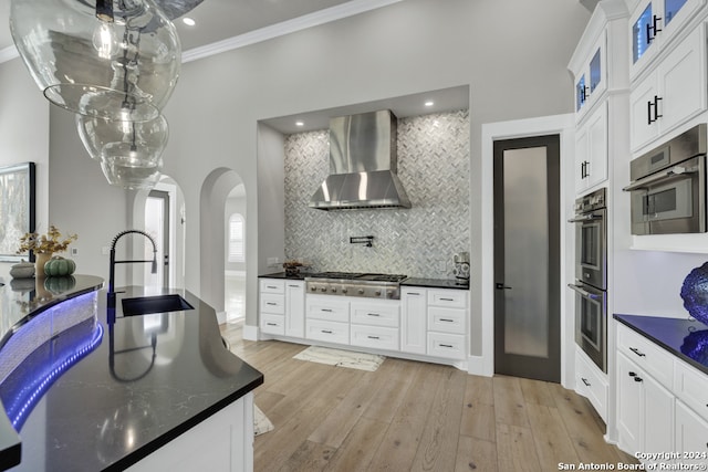 kitchen with white cabinets, appliances with stainless steel finishes, and wall chimney range hood