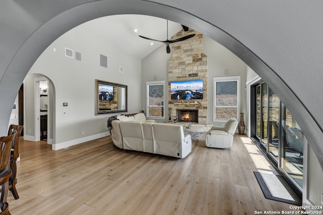 living room with ceiling fan, light hardwood / wood-style floors, a stone fireplace, and high vaulted ceiling