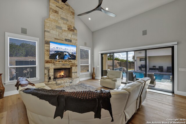 living room with ceiling fan, a stone fireplace, light wood-type flooring, and high vaulted ceiling