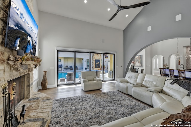 living room featuring ceiling fan, light wood-type flooring, a fireplace, and high vaulted ceiling