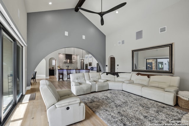 living room with ceiling fan, light hardwood / wood-style flooring, beamed ceiling, and high vaulted ceiling