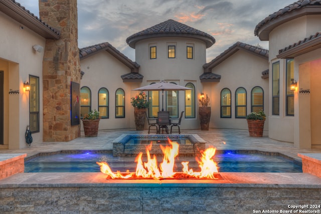 back house at dusk with an in ground hot tub, a patio, pool water feature, and a fire pit