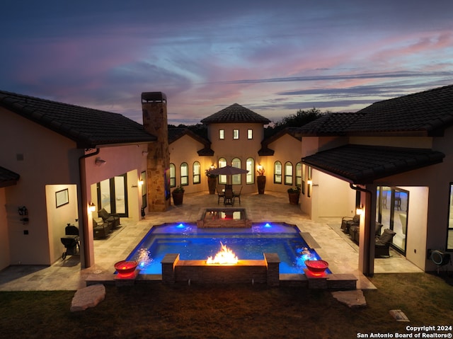 pool at dusk with a patio area, an in ground hot tub, pool water feature, and an outdoor living space with a fire pit