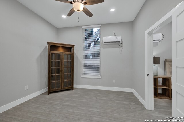 unfurnished room with a wall unit AC, ceiling fan, and light wood-type flooring