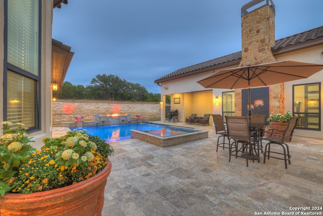 pool at dusk with a patio area, an in ground hot tub, and pool water feature