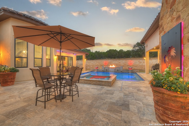 pool at dusk featuring an in ground hot tub, pool water feature, and a patio area