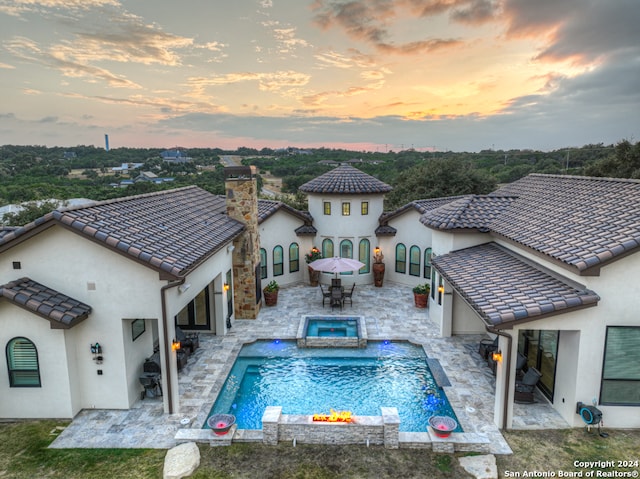 back house at dusk featuring a swimming pool with hot tub and a patio