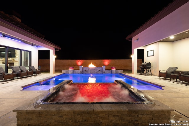 pool at night with a fire pit, a grill, pool water feature, a patio area, and an in ground hot tub