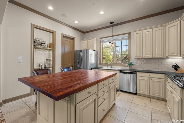 kitchen with wood counters, stainless steel appliances, sink, cream cabinets, and hanging light fixtures