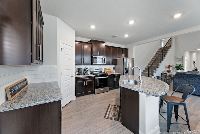 kitchen with sink, light stone countertops, stainless steel appliances, and light hardwood / wood-style flooring