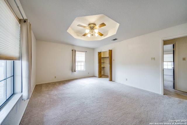 empty room with ceiling fan, a raised ceiling, and light carpet