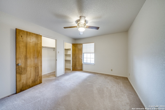 unfurnished bedroom with light carpet, a textured ceiling, ceiling fan, and multiple closets