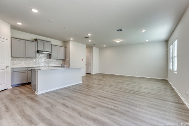 kitchen featuring gray cabinetry, tasteful backsplash, an island with sink, extractor fan, and light wood-type flooring