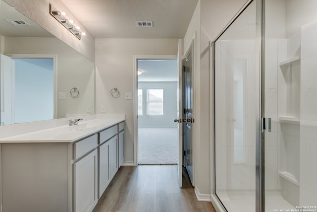 bathroom featuring a shower with shower door, vanity, wood-type flooring, and a textured ceiling