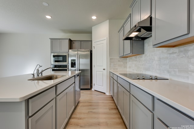 kitchen with sink, light hardwood / wood-style flooring, gray cabinets, tasteful backsplash, and stainless steel appliances