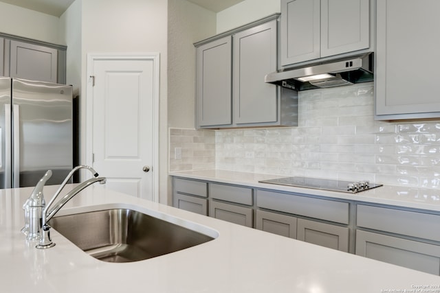 kitchen with gray cabinetry, backsplash, sink, stainless steel fridge, and black electric cooktop