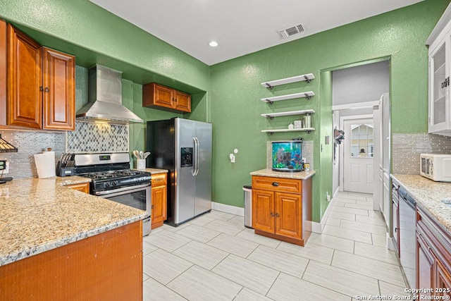 kitchen with decorative backsplash, light stone counters, wall chimney exhaust hood, and appliances with stainless steel finishes