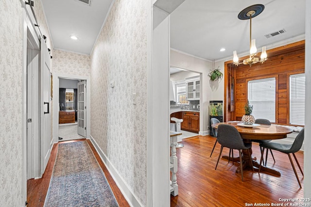 corridor with a barn door, ornamental molding, plenty of natural light, a chandelier, and hardwood / wood-style flooring