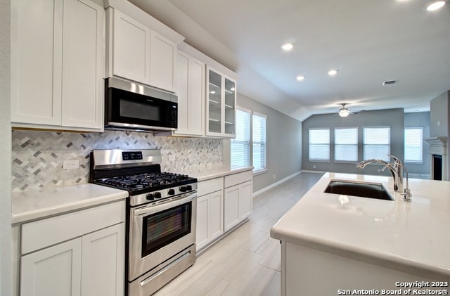 kitchen with sink, plenty of natural light, vaulted ceiling, white cabinets, and appliances with stainless steel finishes