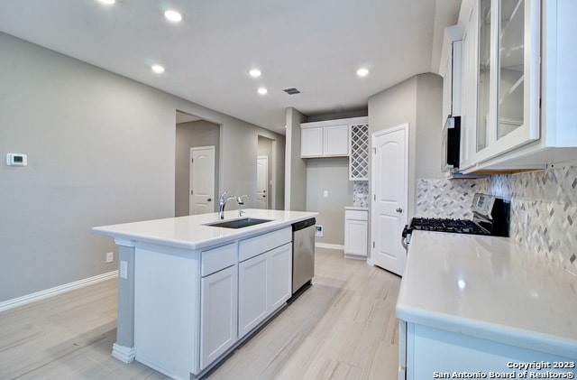 kitchen featuring a kitchen island with sink, white cabinets, sink, light hardwood / wood-style flooring, and appliances with stainless steel finishes