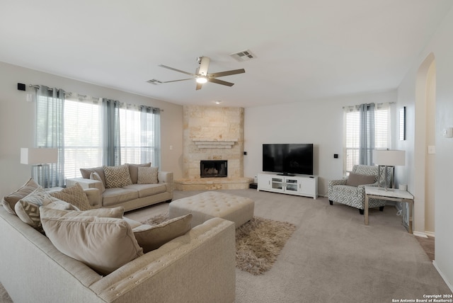 living room featuring light carpet, a stone fireplace, plenty of natural light, and ceiling fan