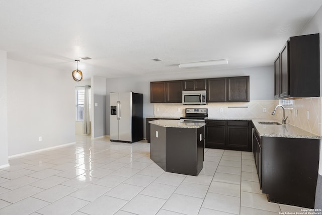 kitchen with decorative backsplash, light stone counters, appliances with stainless steel finishes, a center island, and a sink