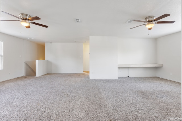 carpeted empty room with visible vents, ceiling fan, and built in desk