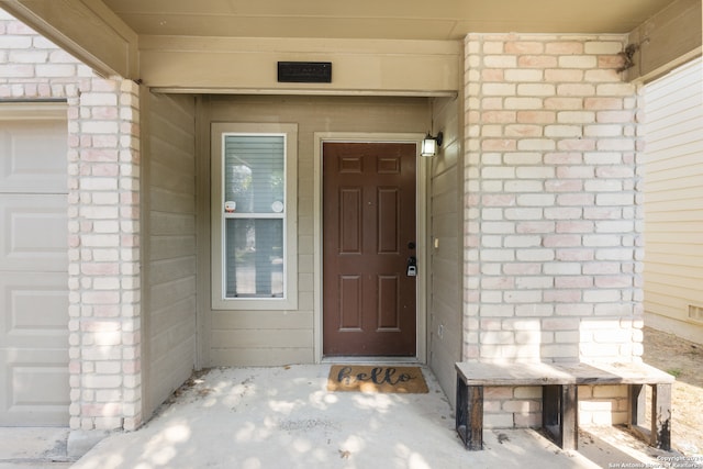 view of exterior entry featuring an attached garage and brick siding